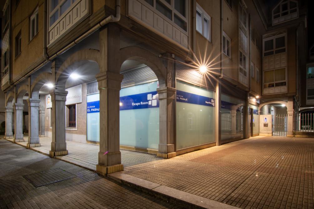 Vista exterior nocturna de la fachada principal de Clínica El Pasaje Escape Room bajo unos arcos de piedra en A Coruña.