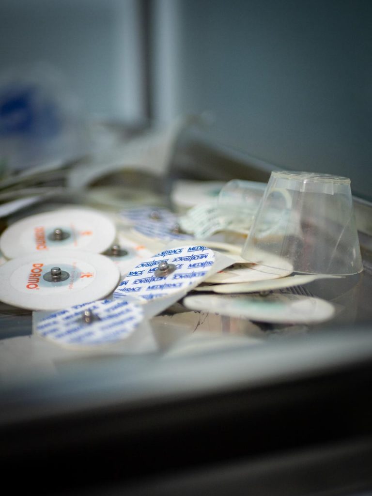 Primer plano de una bandeja médica de acero inoxidable con electrodos ECG y material sanitario, parte de la ambientación realista de Clínica El Pasaje Escape Room en A Coruña.